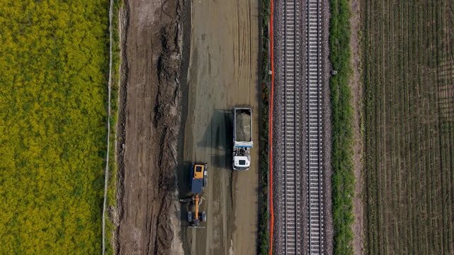 A powerful bulldozer meticulously levels the terrain as a dump truck unloads soil during the construction of a modern high-speed railway in Italy.