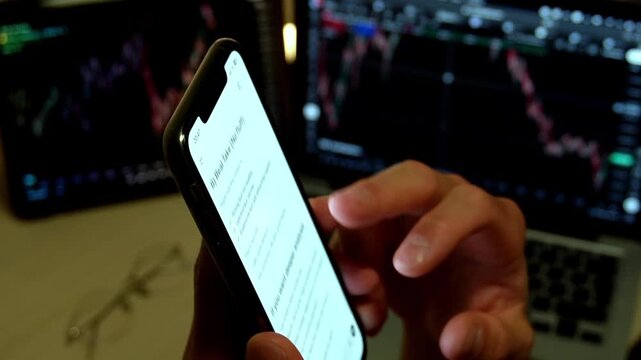 Man hands holding smartphone with AI chatbot showing trading analysis text in front of stock market monitors with charts. Concept of fintech, AI trading assistant, investment and market analysis.