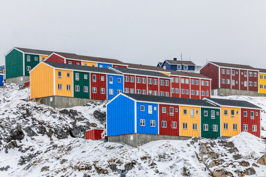 Bright red, orange, green and blue residential buildings with snow-covered rocks and cloudy sky in a Greenlandic town, Sisimiut, Qeqqata, Greenland