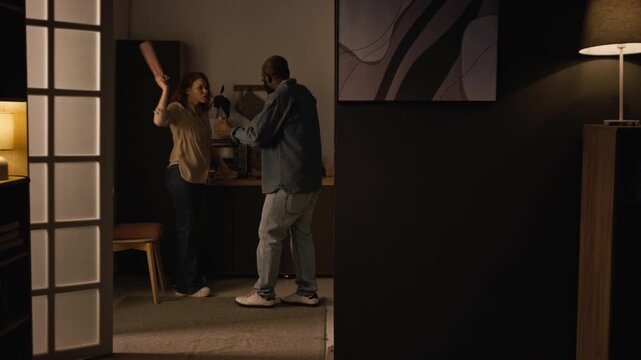 Handheld wide angle shot of multiracial couple fighting in kitchen at home and yelling at each other, childs POV from doorway, copy space