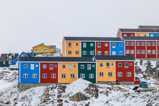 Bright red, orange, green and blue residential buildings with snow-covered rocks and cloudy sky in a Greenlandic town, Sisimiut, Qeqqata, Greenland