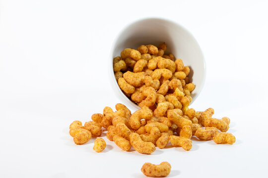 Crunchy peanut flips snacks spilled out from a tipped white ceramic cup onto a clean white background
