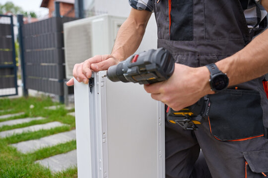 Man fastens white drawer side with cordless drill near grass outside