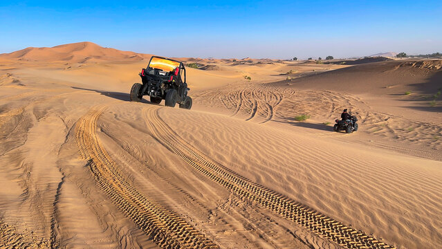 first person point of view from a buggy following a UTV and a quad bike driving up a large golden sand dune in Erg Chebbi in Sahara desert, Merzouga, Morocco