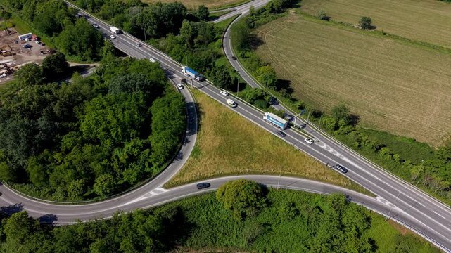 Highway Intersection from Above: An aerial view captures a complex highway intersection on a sunny day, with cars and trucks navigating the roadways amidst lush green trees and fields.