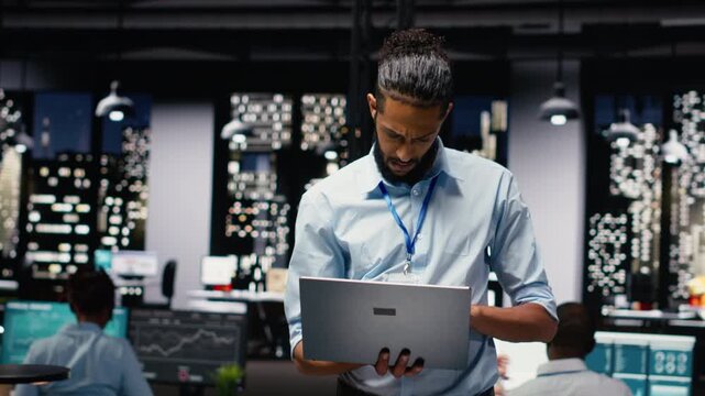 Standing in office, arab manager holds laptop, executive evaluating performance data for operational efficiency. Middle eastern man in workspace late at night finishing accounting tasks.