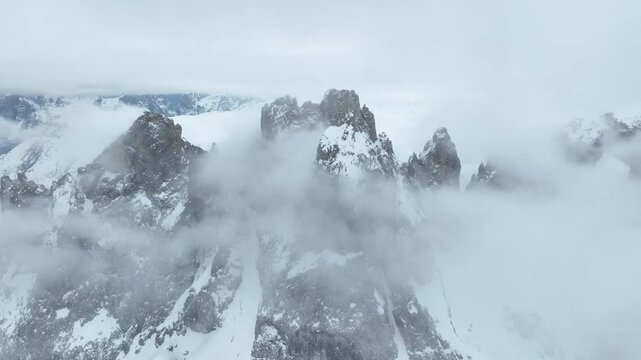 Aerial view of the snow-covered peaks of Parco Naturale Paneveggio Pale di San Martino shrouded in thick clouds in Primiero San Martino di Castrozza, Trentino-Alto Adige, Italy.
