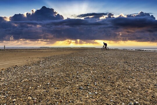 Cyclist on shingle beach, Spurn tidal island, evening sky, Spurn Point peninsula, Hull, Yorkshire, England, United Kingdom