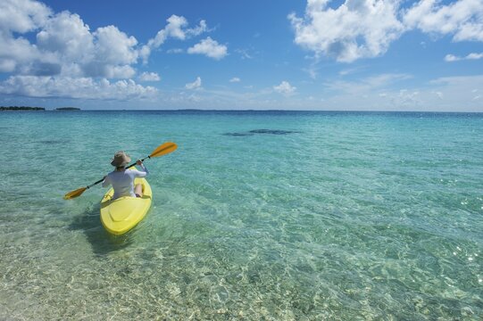 Female tourist kayaking in the turquoise waters of Tikehau, Tuamotu Archipelago, French Polynesia