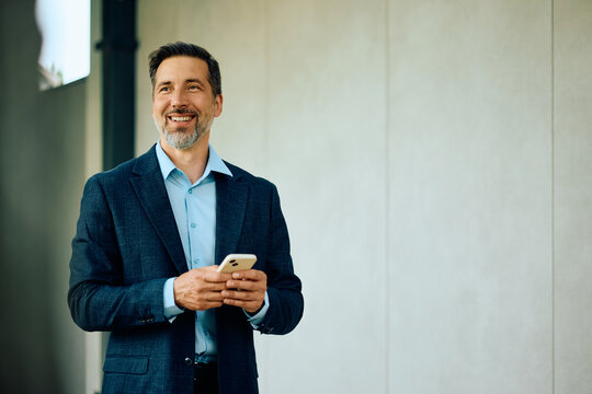 Happy businessman text messaging on cell phone while working in office.
