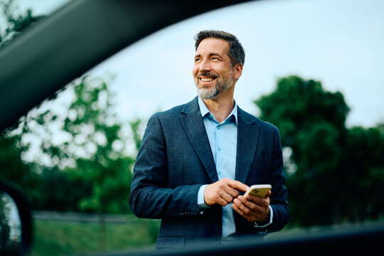 Happy businessman using mobile phone by his car.