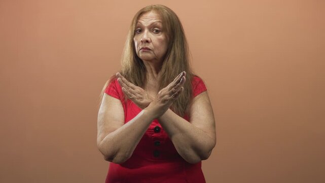 Woman in red dress crossing her hands into an x gesture at chest, forearms and palms visible against a plain studio backdrop; defiance refusal.