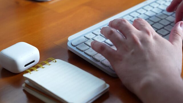 A man typing on a white computer keyboard on a wooden desk