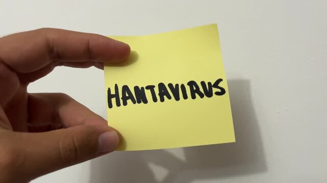 Hand holding sticky note with Hantavirus warning written in black marker