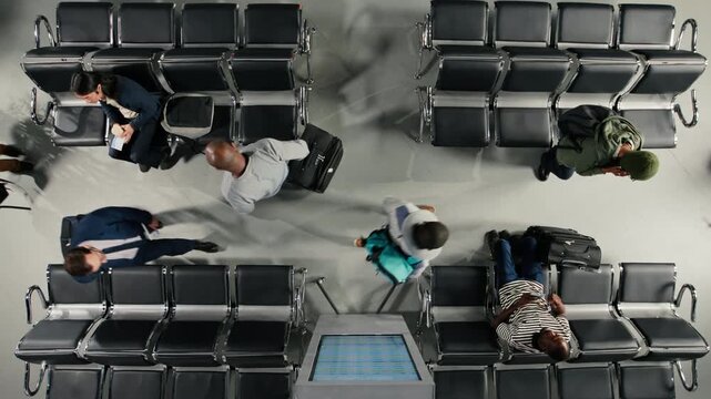 Multiethnic travelers reading plane departure time schedule on screen in airport terminal, top down view. Men and women waiting on benches to fly home during holiday rush, checking timetable