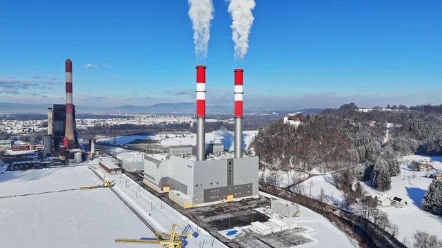 Aerial view of Mellach Power Plant with smoking chimneys in a snowy winter landscape under a clear blue sky in Wildon, Styria, Austria.