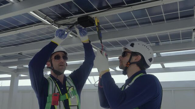 Engineers maintenance solar panels rooftop green energy installation with electrical wiring safety checks technician and technicians work under daylight on roof array, perform multimeter test