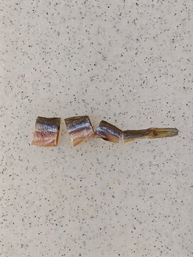 Salty dried smelt fish pieces meticulously arranged on a speckled light gray and white countertop, forming the punctuation mark dash, creating a unique culinary composition and a delicious savory