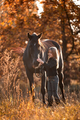 A beautiful girl walks with a brown horse in golden autumn
