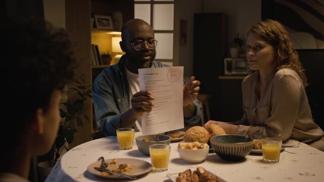 Medium shot of parents looking at exam papers with bad grades and scolding child while sitting at dinner table at home, family conflict scene lit by low evening light