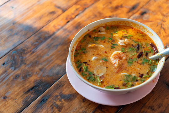 Traditional Thai tom yum goong shrimp herbs spicy sour broth served hot in bowl on wooden table