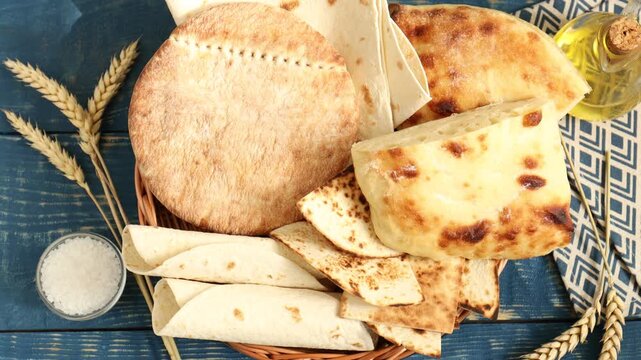 Tasty pita bread and lavash in wicker basket spinning on blue wooden table, flat lay