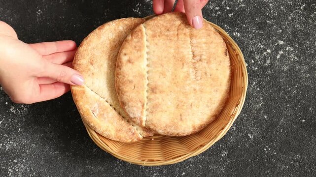 Woman putting tasty pita bread into wicker basket at grey table, top view