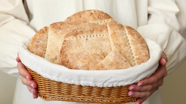 Woman holding wicker basket with tasty pita bread on light background, closeup