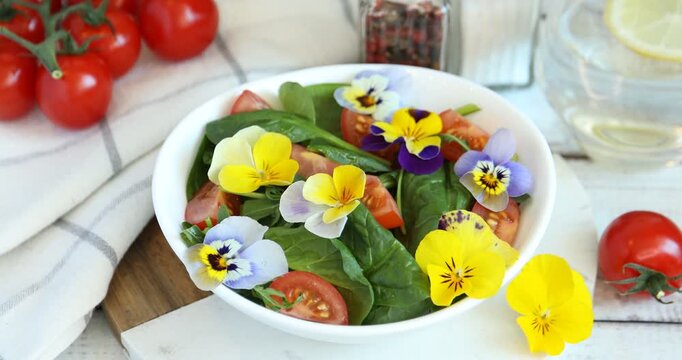 Woman putting pansy flower into bowl with fresh salad white wooden table, closeup