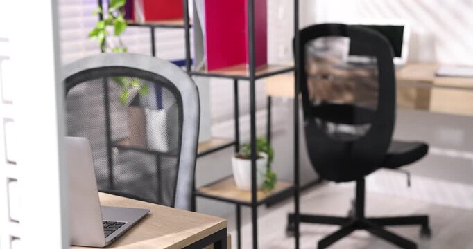 Interior design. Wooden desks with laptops, stationery, plants and shelving unit in office, closeup. Camera moving in