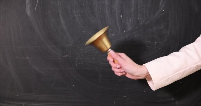 School holidays. Teacher ringing golden bell near chalkboard, closeup