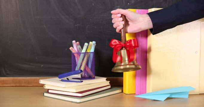 School holidays. Teacher ringing golden bell, paper plane and stationery near chalkboard, closeup