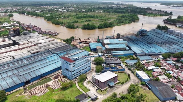 Aerial view of a plywood factory with stacks of logs in front of it as raw material for plywood production