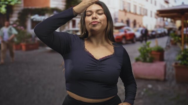 Woman plus size shielding eyes with hand on cobblestone street, smiling with nose ring and exposed midriff, casual daytime scene; carefree joy.