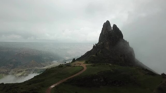 Semicircular camera movement filming the Muela del Diablo located in La Paz, Bolivia, a mountain shaped like a molar tooth. On a cloudy day, with drizzle and some fog.