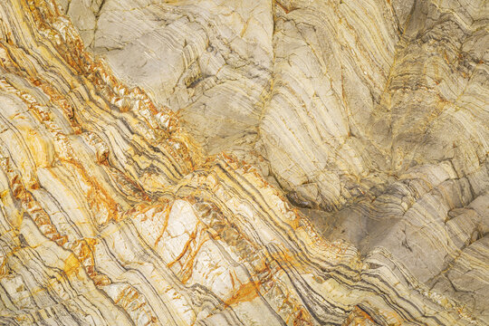 View of the intricate geological layers and folded rock formations at Silence Beach, featuring vibrant orange and beige mineral veins in Asturias, Asturias, Spain.
