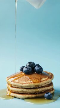 Golden syrup cascading over stacked pancakes topped with fruit cubes on a pastel background 