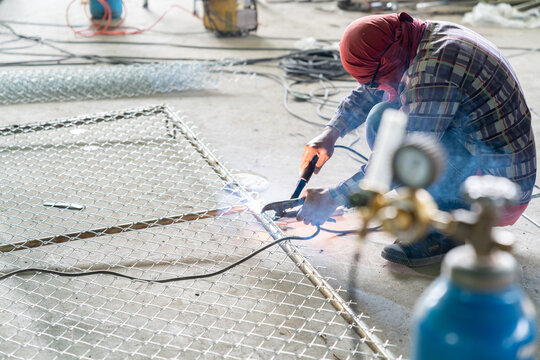 Professional welder joining a galvanized steel wire mesh to a metal frame in an industrial workshop.