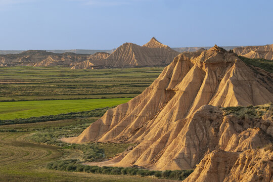 View of the unique sandstone rock formations and arid badlands of Bardenas Reales with green fields in the foreground in Navarre, Navarre, Spain.
