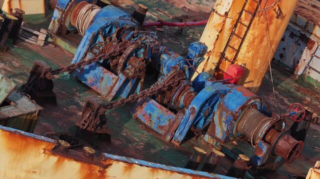 Rusty abandoned ship deck detail with old winches and anchor chains slowly moving during daytime.