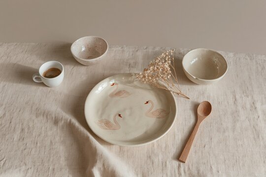 Cream linen tablecloth background serves as a setting for swan motif ceramic tableware and coffee cup for home textile design, kitchenware marketing and cafe branding