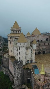 Vertical screen, Vietnam, Da Nang, Ba Na Hills Misty Aerial View Ba Na Hills Castle, Da Nang Vietnam Fog Envelops Stone Towers And Turrets, Medieval Fortress Perched On Lush Mountain,
