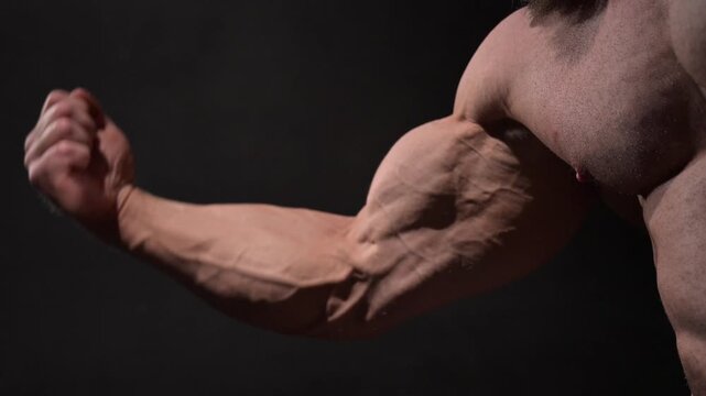 A male bodybuilder poses in shorts, showing off his arm muscles.