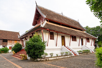 Obraz premium Side View of Historic Lao Buddhist Temple with Long Wooden Roof, White Walls and Golden Lion Statues in Luang Prabang