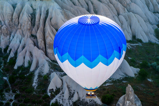 Aerial view of a blue and white hot air balloon with people in the basket flying over the unique rock formations and valleys of Cappadocia Kayseri, Kayseri, Turkiye.