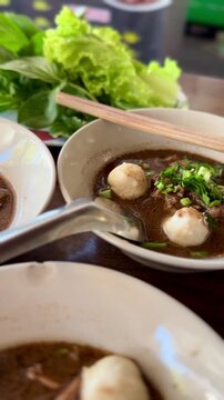 Authentic Thai boat noodle soup with pork meatballs and fresh herbs