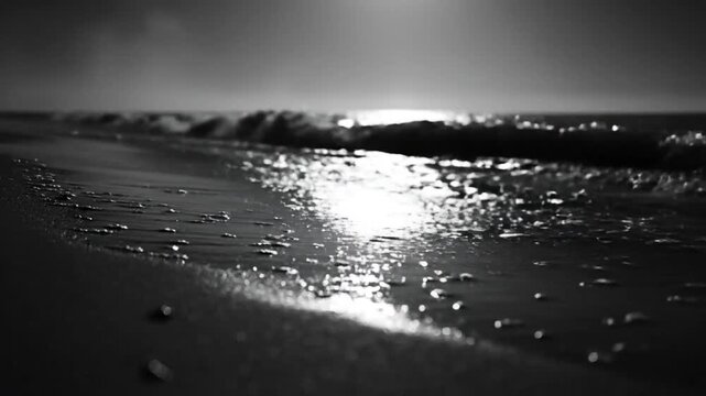 Black and white close up of gentle waves lapping on the sandy beach under the sunlight