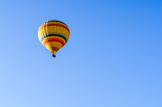 Aerial view of a colorful yellow and red striped hot air balloon floating in a clear blue sky over the landscape of Cappadocia Kayseri, Kayseri, Turkiye.