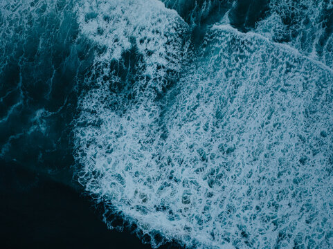 Aerial view of crashing ocean waves with white foam and deep blue water at La Jolla Cove, San Diego, California, United States.