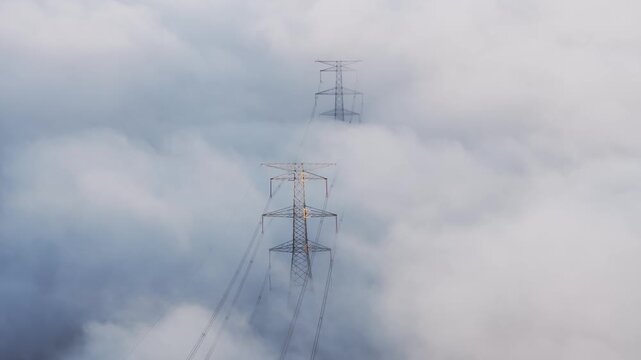 High voltage transmission towers standing amidst thick clouds and fog